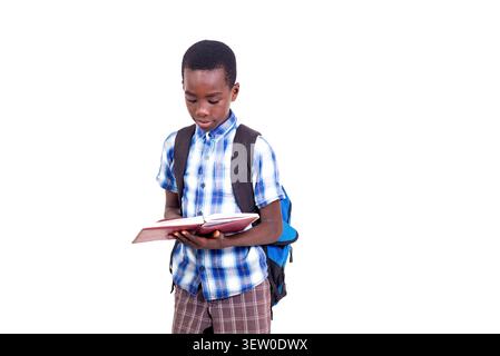 pupil in checkered shirt standing on white background wearing backpack reading a book. Stock Photo