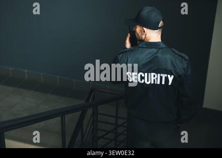 Bodyguard in uniform using walkie talkie while walking down stairs indoors, space for text Stock Photo