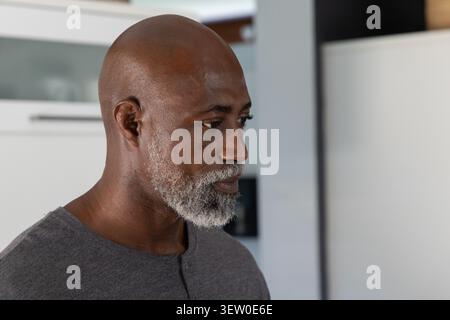 African American man standing, looking right in kitchen with white cabinets, wearing gray shirt Stock Photo