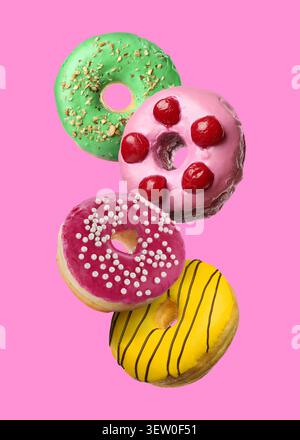 Yummy donuts covered with icing falling on pink background Stock Photo