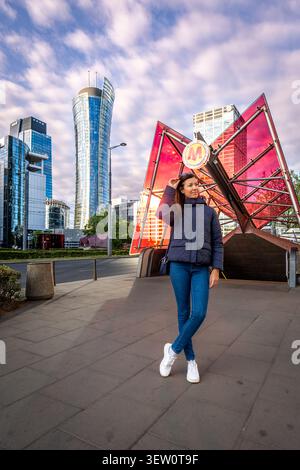 Young woman standing near Warsaw metro entrance in skyline district under golden light with clouds Stock Photo