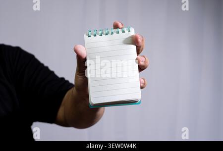 Male hand holds an open, blank lined notebook with a teal spiral binding, presenting empty pages against a plain grey background, showing details of f Stock Photo