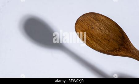 Close up view of a smooth carved wooden spoon bowl suspended diagonally over a solid white background, casting a distinct soft rounded shadow that hig Stock Photo