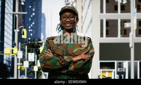 Strolling on sidewalk downtown, city street and happy army soldier admiring skyscrapers on avenue. Black officer enjoying military leave and sightseeing in the metropolitan area. Stock Photo
