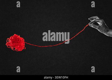 Hand Pulling Red String from Tangled Yarn Ball in Black and White on Textured Paper Background Stock Photo