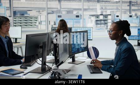 Developer uses artificial intelligence to examine microchip circuit layout in factory RD office. African american employee uses AI tech to improve semiconductors manufacturing, camera A Stock Photo