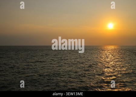 Natural dramatic sunset over tropical ocean horizon during golden hour. Warm orange sky reflecting on sea water waves with open space context. Stock Photo