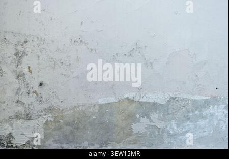 Close-up of a severely weathered white exterior wall showing multiple layers of peeling paint, water damage staining and greenish mould patches. Stock Photo