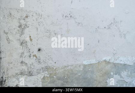 Close-up of an exterior white plaster wall with a prominent horizontal band of severely peeling and flaking paint revealing multiple painted layers. Stock Photo