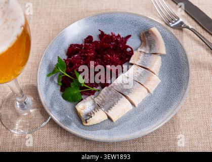 On round blue plate - lightly salted herring fillet cut into pieces with stewed beets Stock Photo