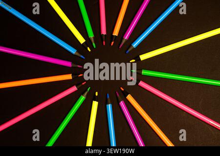 Top view of bright colored pencils arranged in a circular pattern on a black background, creative back to school and stationery concept. Stock Photo