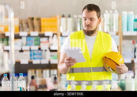 Man builder in yellow vest with medical prescription in hand looking for medicine in pharmacy Stock Photo