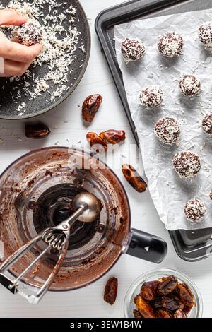 A hand rolling an energy ball in shredded coconut with ingredients around. Stock Photo