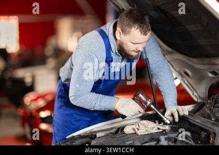 Man auto mechanic repairing engine under hood of car in garage Stock Photo