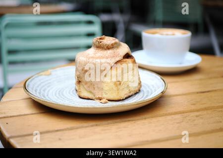 Cinnamon Roll served on a white plate beside a cup of coffee at a cafe Stock Photo