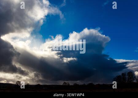Massive cumulonimbus clouds fill the autumn sky, casting dark, ominous shadows. Intense sunrays pierce through the storm's edge, revealing nature's ra Stock Photo