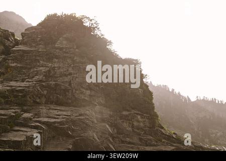 Sunlight breaks through mist over a rocky mountain slope in Washington’s Cascades, highlighting the rough texture of stone and scattered evergreens. Stock Photo