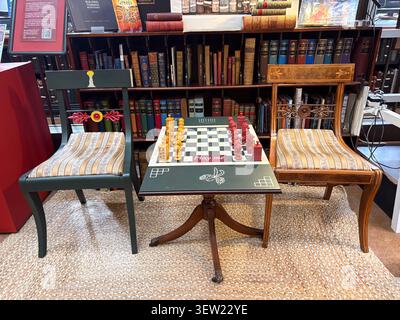 Chess board with red and yellow pieces on a table between two chairs at The Portico Library in Manchester UK, set against library bookshelves. Stock Photo