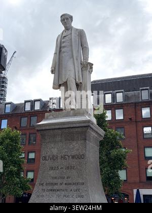 A stone statue of Oliver Heywood in Albert Square, Manchester, UK, against a backdrop of Victorian-style brick architecture. Stock Photo