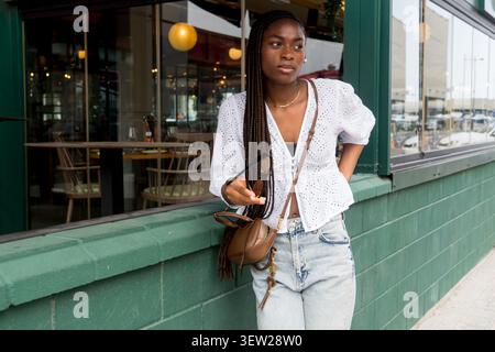 beautiful young woman with an afro hairstyle made of braids, outside a restaurant with a green facade Stock Photo
