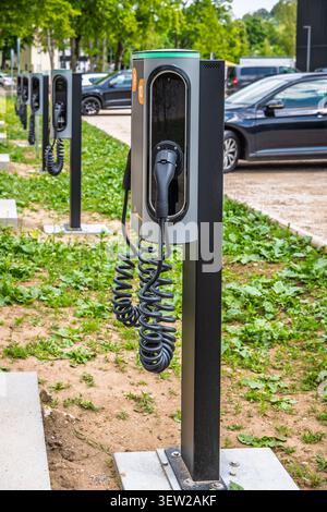 Modern electric car charging posts with cables ready for use in a green outdoor setting with vehicles parked nearby Stock Photo