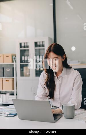 Young businesswoman professional employee using pc doing online banking analysing at workplace. Asian middle-aged business woman working on laptop com Stock Photo