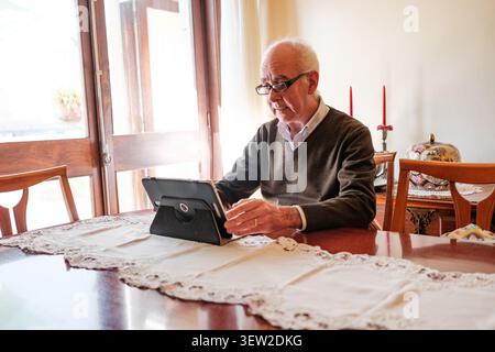 Senior man sitting at a table interacting with a tablet computer Stock Photo