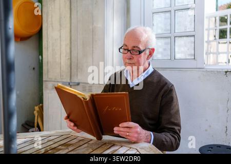 Elderly man looking at old photographs in a photo album, reminiscing about the past Stock Photo