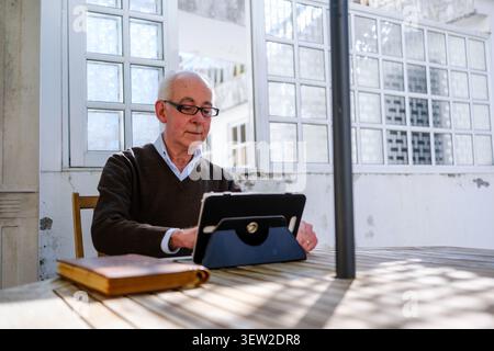 Senior man working on a tablet at an outdoor wooden table Stock Photo