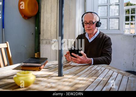 Senior man listening to music or podcast using smartphone and headphones outdoors Stock Photo