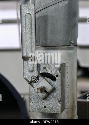 Detailed closeup of galvanized metal latch and hinge assembly mounted on vertical post, showing textured zinc finish, rivets, nut, wing nut, and adjus Stock Photo