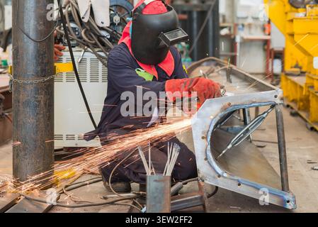 Man with protective gear working on a screw conveyor trough using an angle grinder. Stock Photo