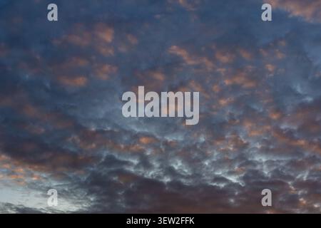 Dramatic sunset cloudscape with dark grey turbulent cloud formations lit by warm orange and amber light from below Stock Photo