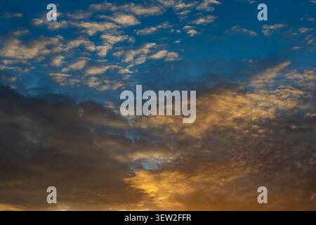 Vivid sunset cloudscape with golden amber light in the lower sky and small white clouds scattered across a deep blue upper sky Stock Photo