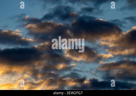 Dark brooding clouds lit from below by golden light against a blue sky at sunset Stock Photo