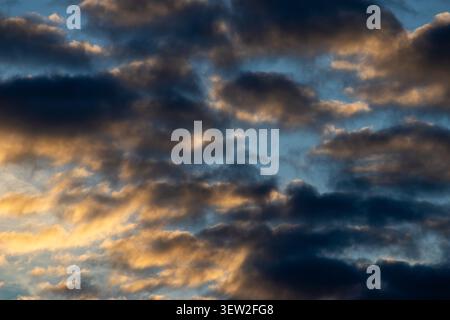 Dark brooding clouds lit from below by golden light against a blue sky at sunset Stock Photo