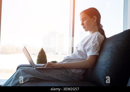 Young woman working remotely on laptop at window home Stock Photo