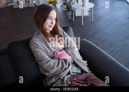 Young woman day dreaming on couch wrapped in blanket Stock Photo