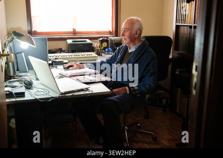 Senior man in robe using computer at his home desk, enjoying retirement Stock Photo