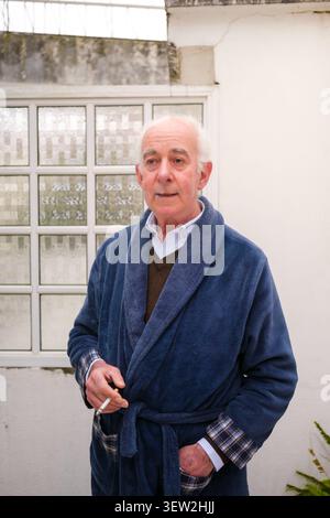 Elderly man standing outdoors in his bathrobe and shirt, holding a cigarette Stock Photo