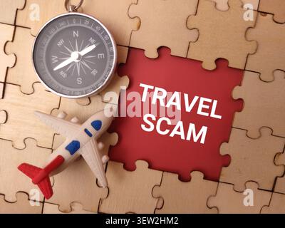 A toy airplane and a compass rest on a jigsaw puzzle around a red opening containing the words TRAVEL SCAM. Stock Photo