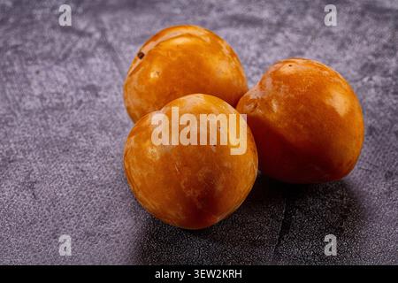 Three glossy yellow plums arranged on dark gray textured background. Warm lighting highlights fruit texture natural imperfections. Rich orange yellow Stock Photo