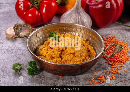 Rich orange lentil curry served in ornate hammered copper bowl. Fresh parsley garnish. Red bell peppers garlic in background. Scattered red lentils on Stock Photo