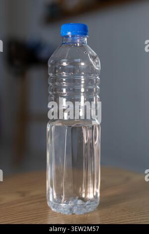 Partially Filled Clear Plastic Water Bottle with Blue Cap on Wooden Table Stock Photo