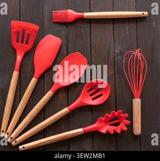 Red Silicone Kitchen Utensils with Wooden Handles on Dark Wooden Background Stock Photo