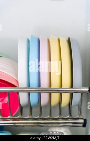 Organized colorful plates and cups in a modern kitchen dish rack. Clean, organized kitchen cabinet featuring a dish drying rack filled with colorful bowls, plates, and mugs, highlighting efficient home organization and kitchen management. Stock Photo