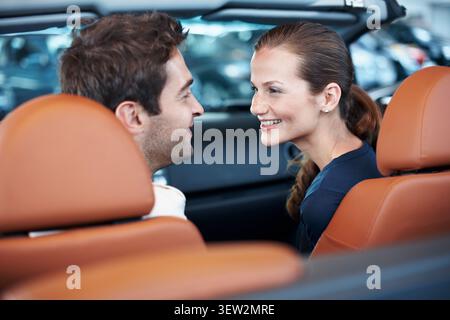 Back, car dealership and happy couple in convertible for decision, purchase or test drive. Choice, love and satisfaction with people in showroom Stock Photo