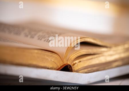 Open Bible on the altar of a church with selective focus on the gold edging of the paper pages. Atmospheric still life of the Book of Books of Christi Stock Photo
