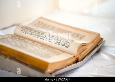 Open Bible on the altar of a church with selective focus on the gold edging of the paper pages. Atmospheric still life of the Book of Books of Christi Stock Photo