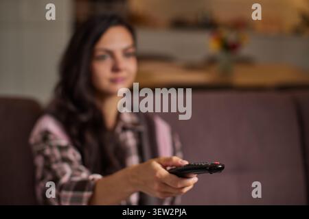 Woman holding a remote control, enjoying entertainment and leisure time in her house, focus on remote control Stock Photo